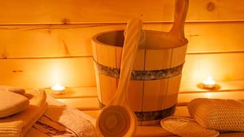 Un balde de madera con un mazo de madera, toallas y una vela sobre un banco de madera.