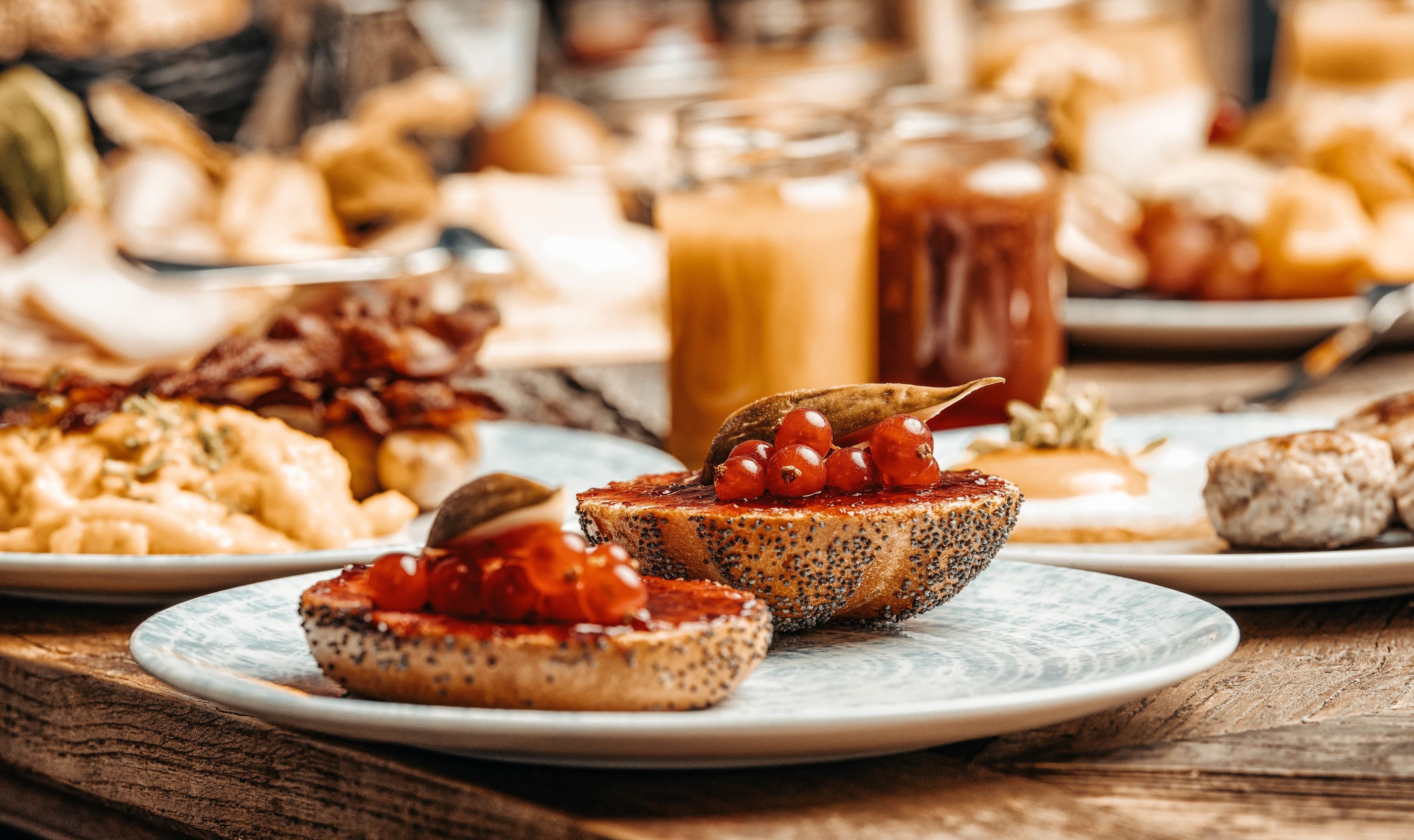 Una mesa con diversos alimentos, entre ellos tostadas con bayas rojas y un tarro de té helado.