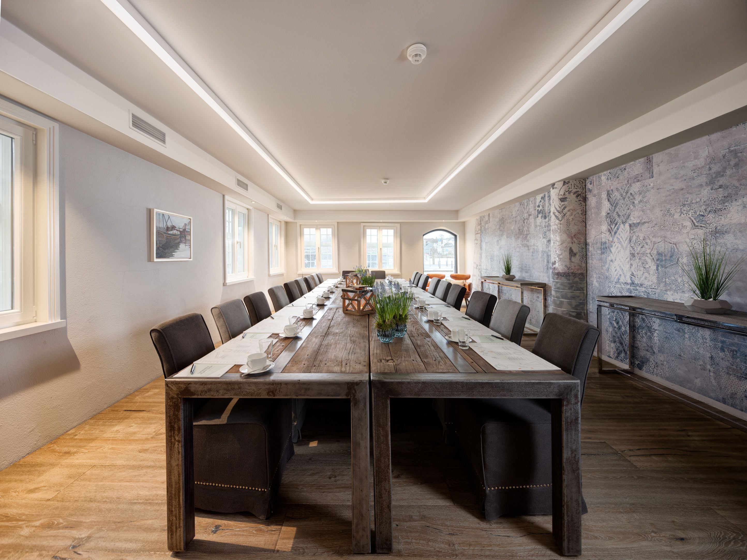 A conference room with a long wooden table, multiple chairs, and a marble wall.