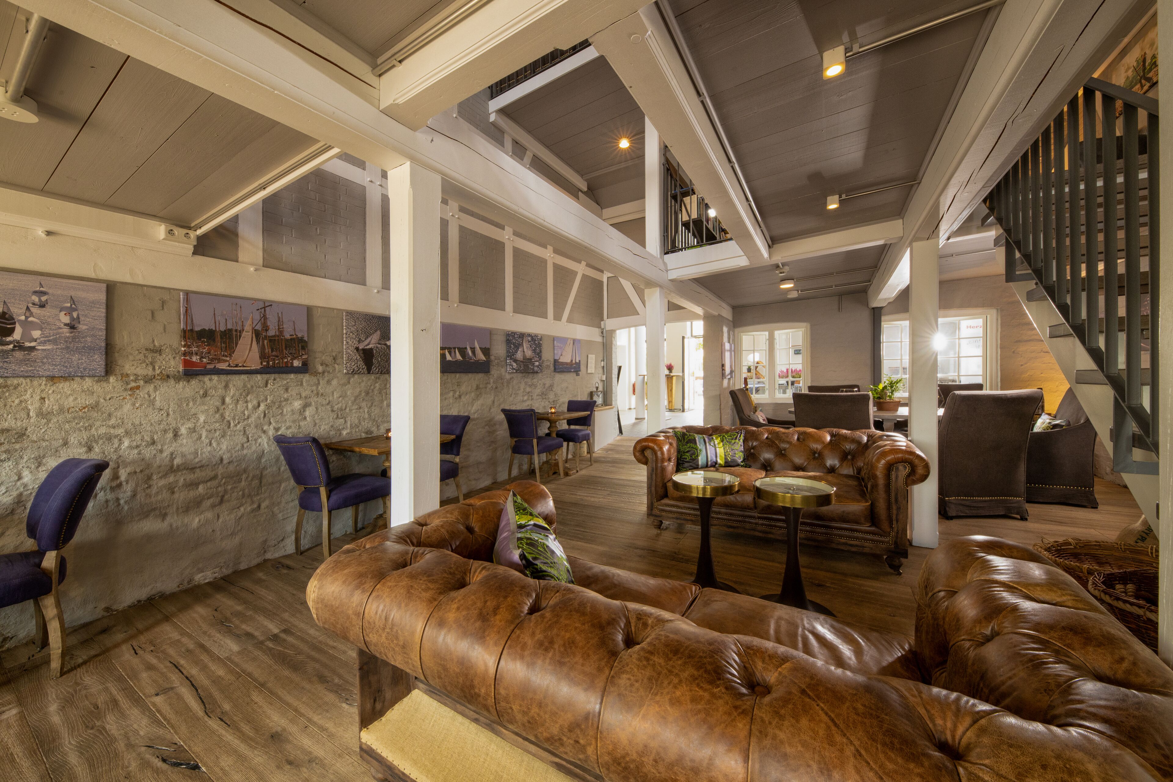 Un vaste espace de détente avec des canapés en cuir, un plancher en bois et un plafond haut avec des poutres apparentes.
