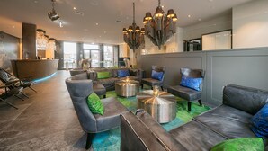 A modern lounge area with leather sofas, a reception desk, and a large window offering a city view. - Hotel Hafen Flensburg (Flensburg)