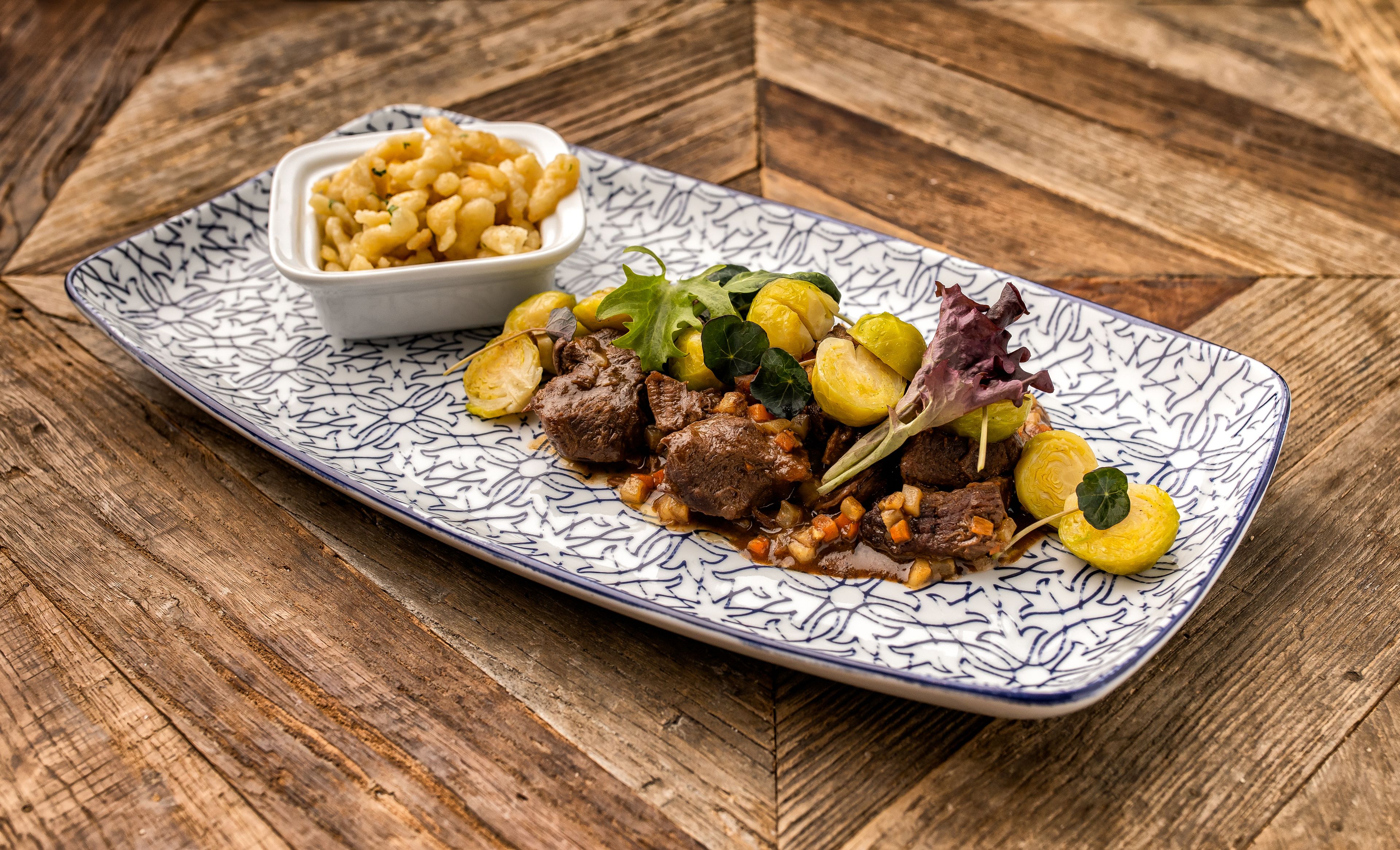 A rectangular plate with a blue and white pattern, containing a dish of meat and vegetables, and a small bowl of what appears to be a side dish.