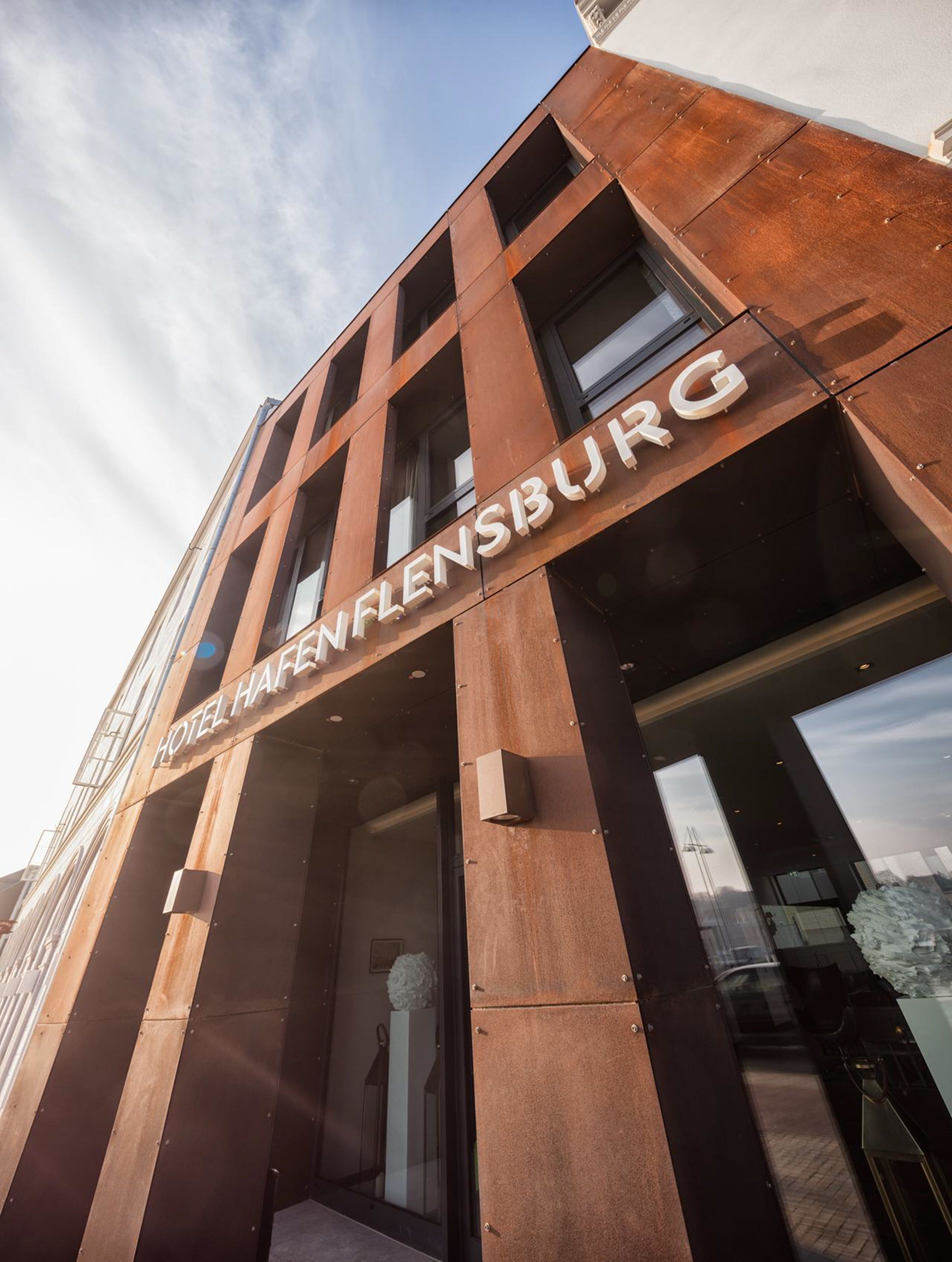 The exterior of Hotel Hafenflensburg with a modern architectural design, featuring large windows and a prominent entrance.