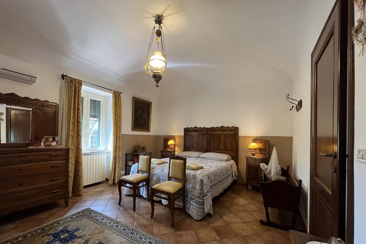 A bedroom with a wooden bed, two bedside tables with lamps, a dresser, a chair, a rug, and a ceiling fan.