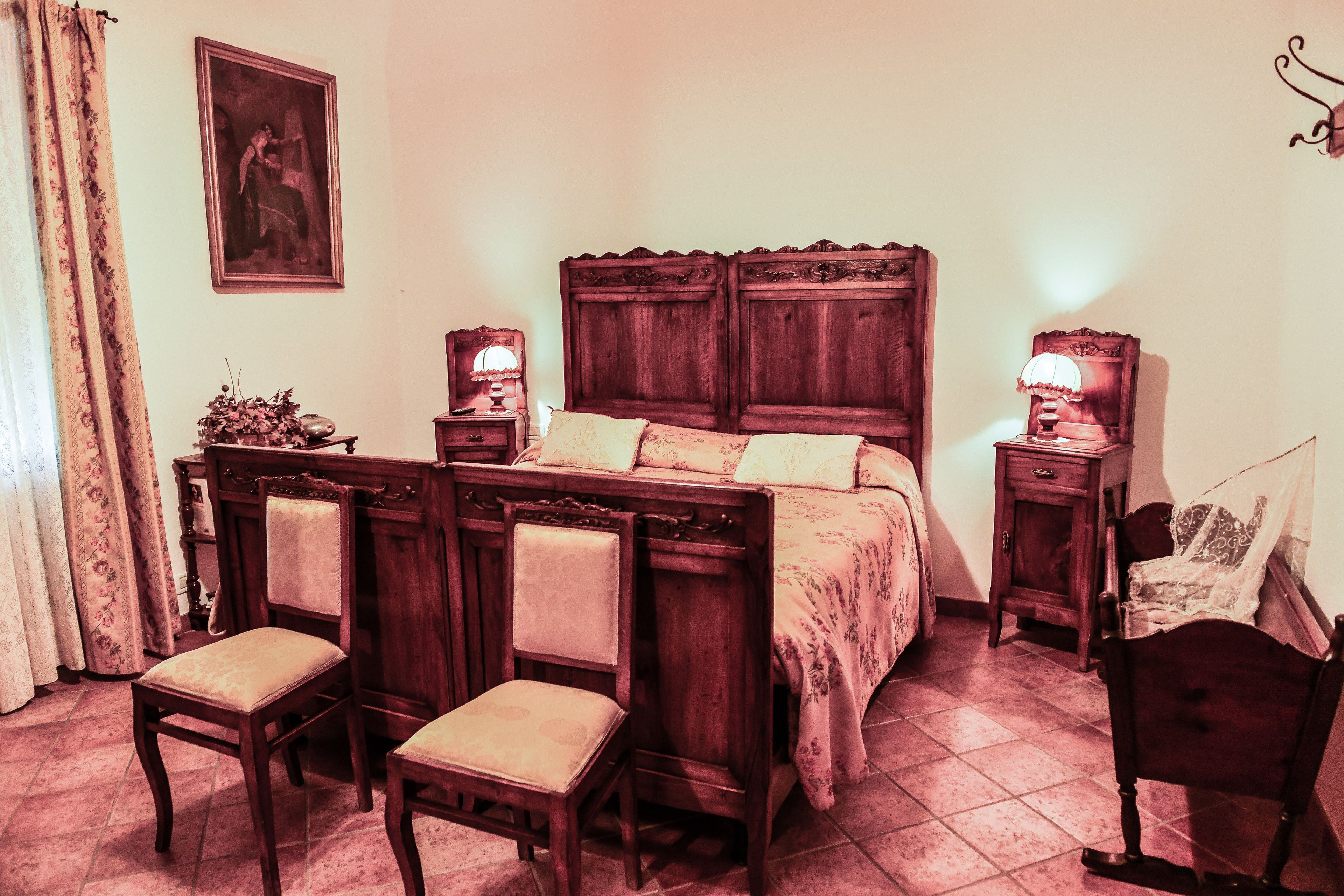 Un dormitorio con una cama de madera, dos mesitas de noche con lámparas, una silla y un cuadro en la pared.