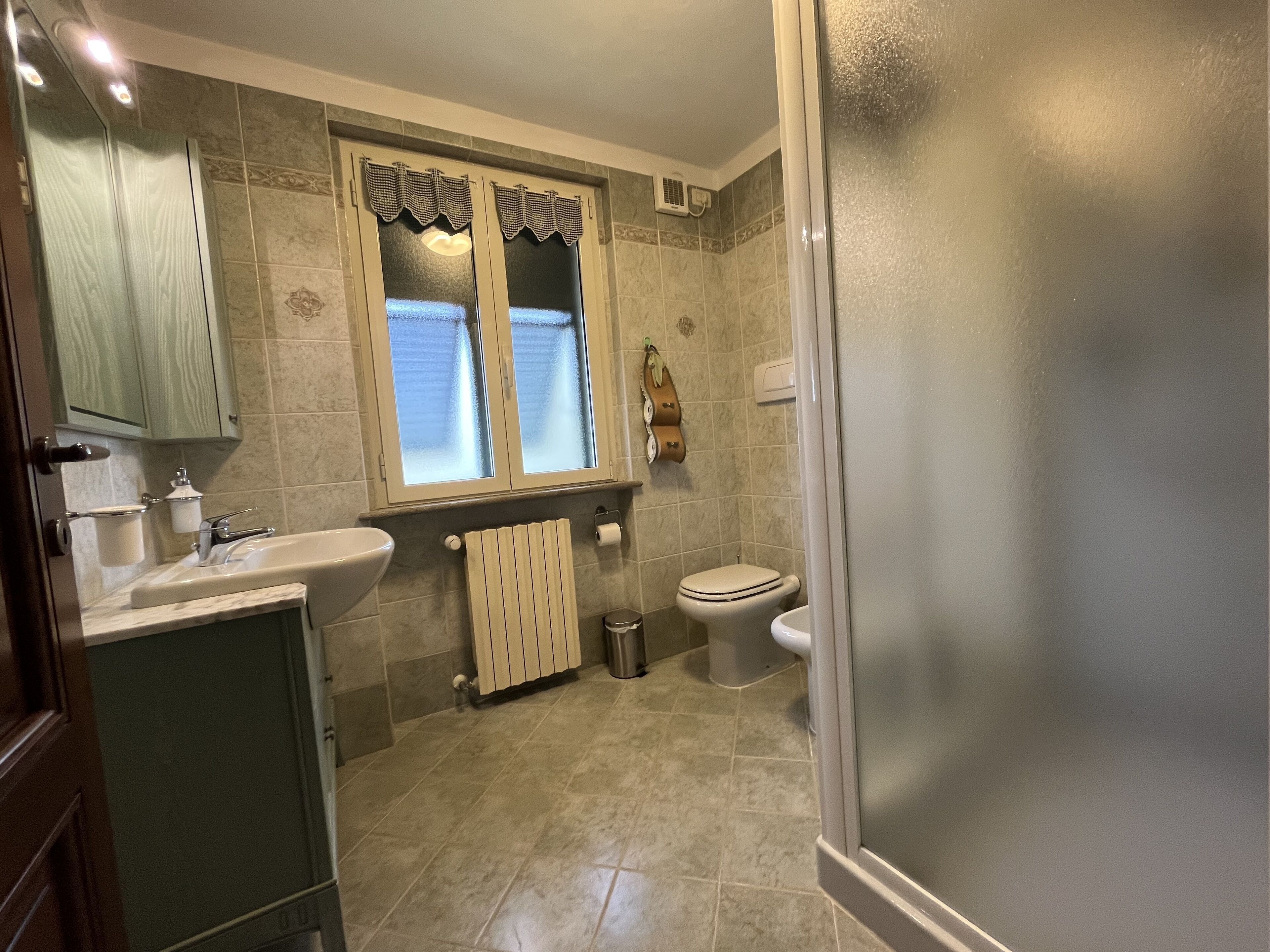 Une salle de bain équipée d’un lavabo, de toilettes et d’une fenêtre agrémentée d’une lambrequin décorative.