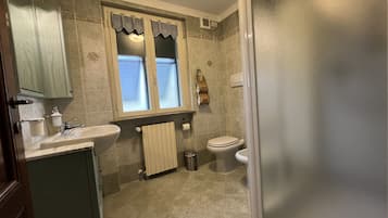 Une salle de bain équipée d’un lavabo, de toilettes et d’une fenêtre agrémentée d’une lambrequin décorative.