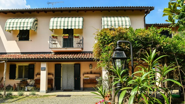 A two-story building with a balcony, a gravel driveway, and a garden with plants and a lamp post. - Cascina Folletto (Pozzolo Formigaro)