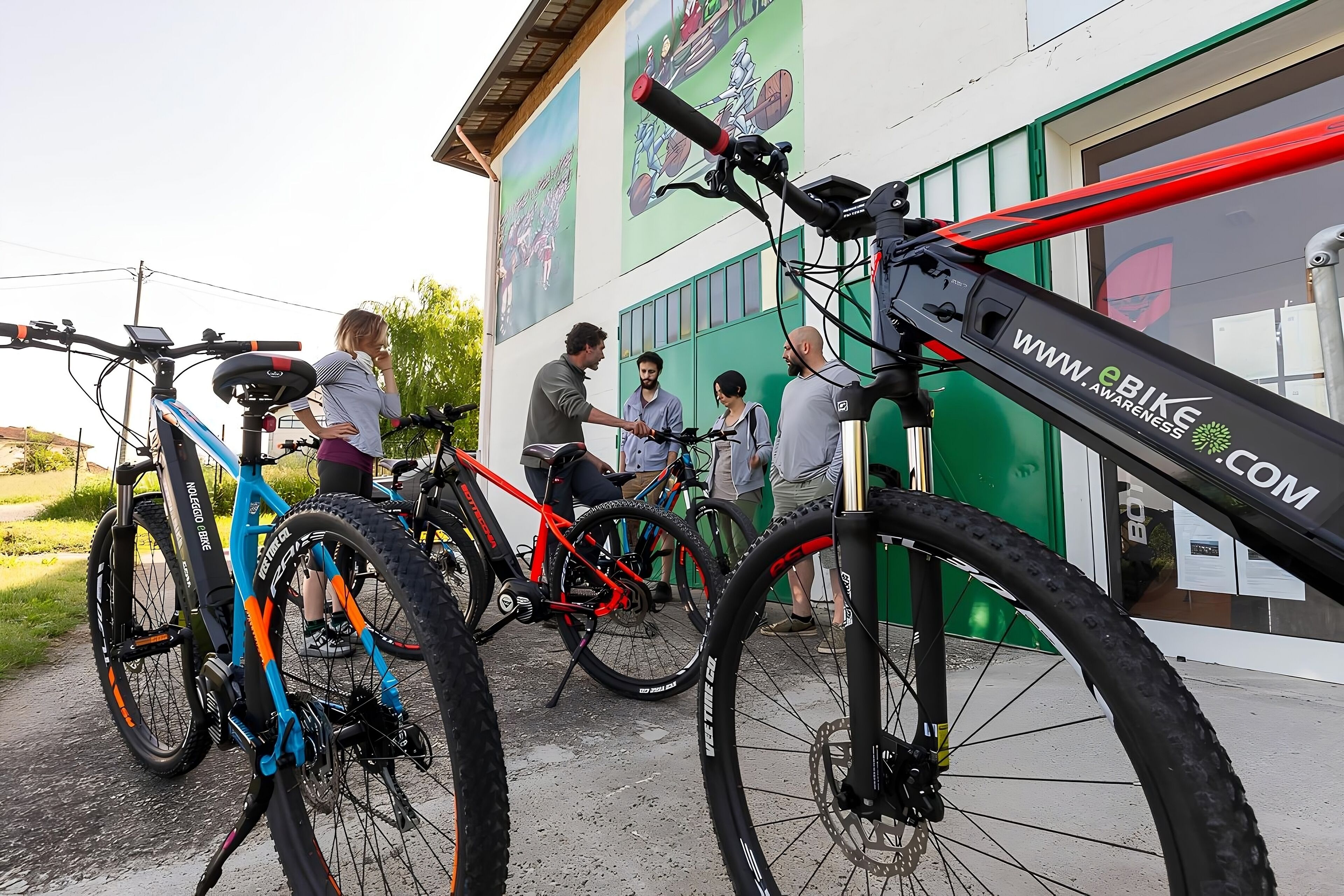 Un groupe de vélos est garé devant un immeuble dont la porte est verte et dont le mur est décoré d’une fresque.