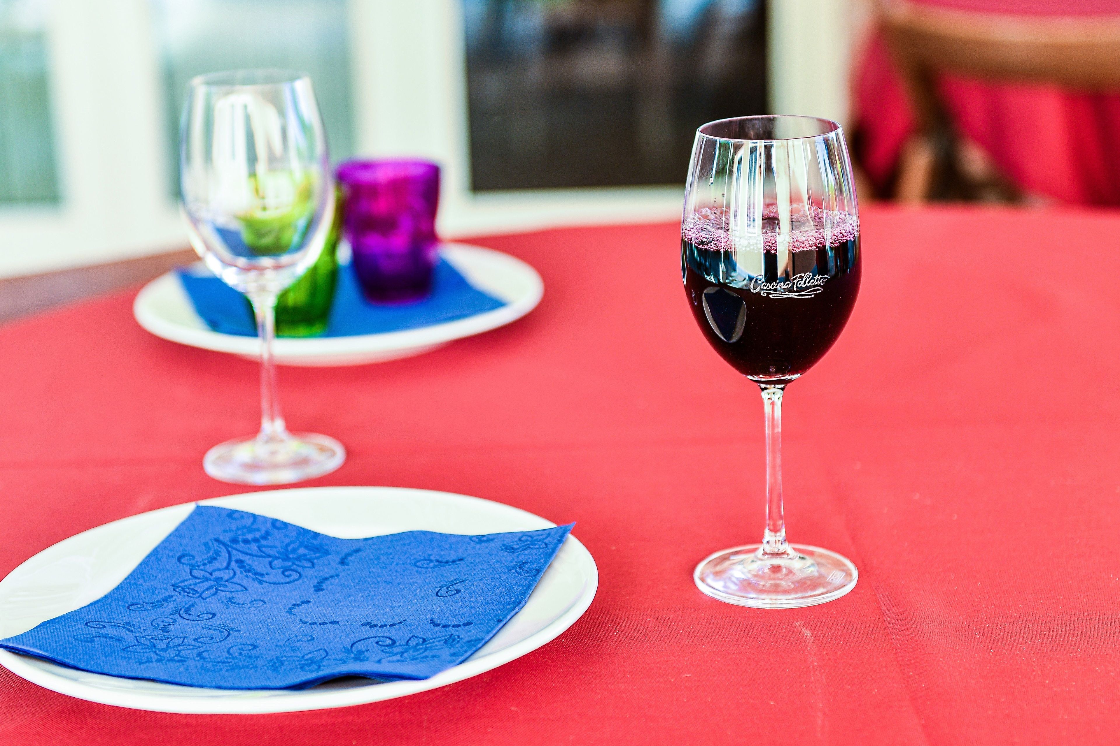 A table with a red tablecloth, a glass of red wine, and a blue napkin on a white plate.