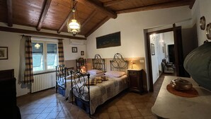 A cozy bedroom with a wooden ceiling, a bed with a headboard, a bedside table, a window with curtains, and a radiator. - Cascina Folletto (Pozzolo Formigaro)
