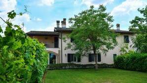 A two-story building with a tiled roof, a balcony, and a well-maintained garden with a tree and grass. - Cascina Folletto (Pozzolo Formigaro)