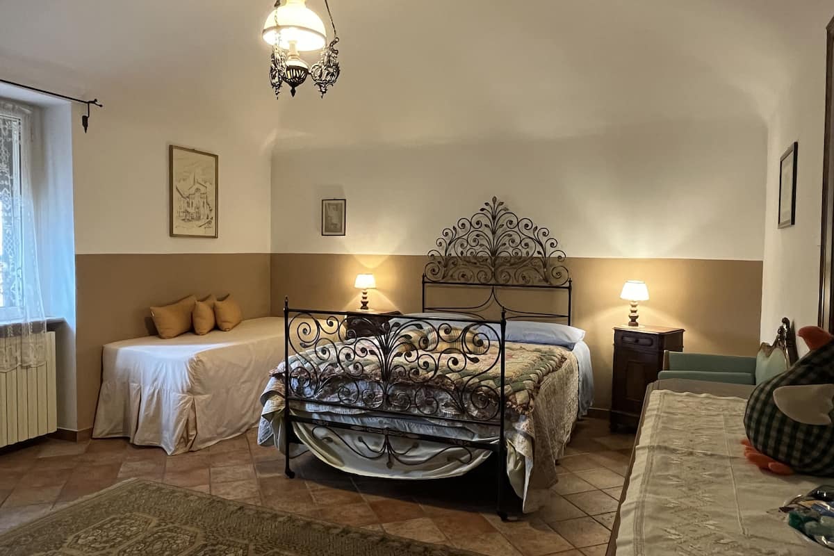 A bedroom with a four-poster bed, two bedside tables with lamps, a window with a curtain, and a patterned rug.