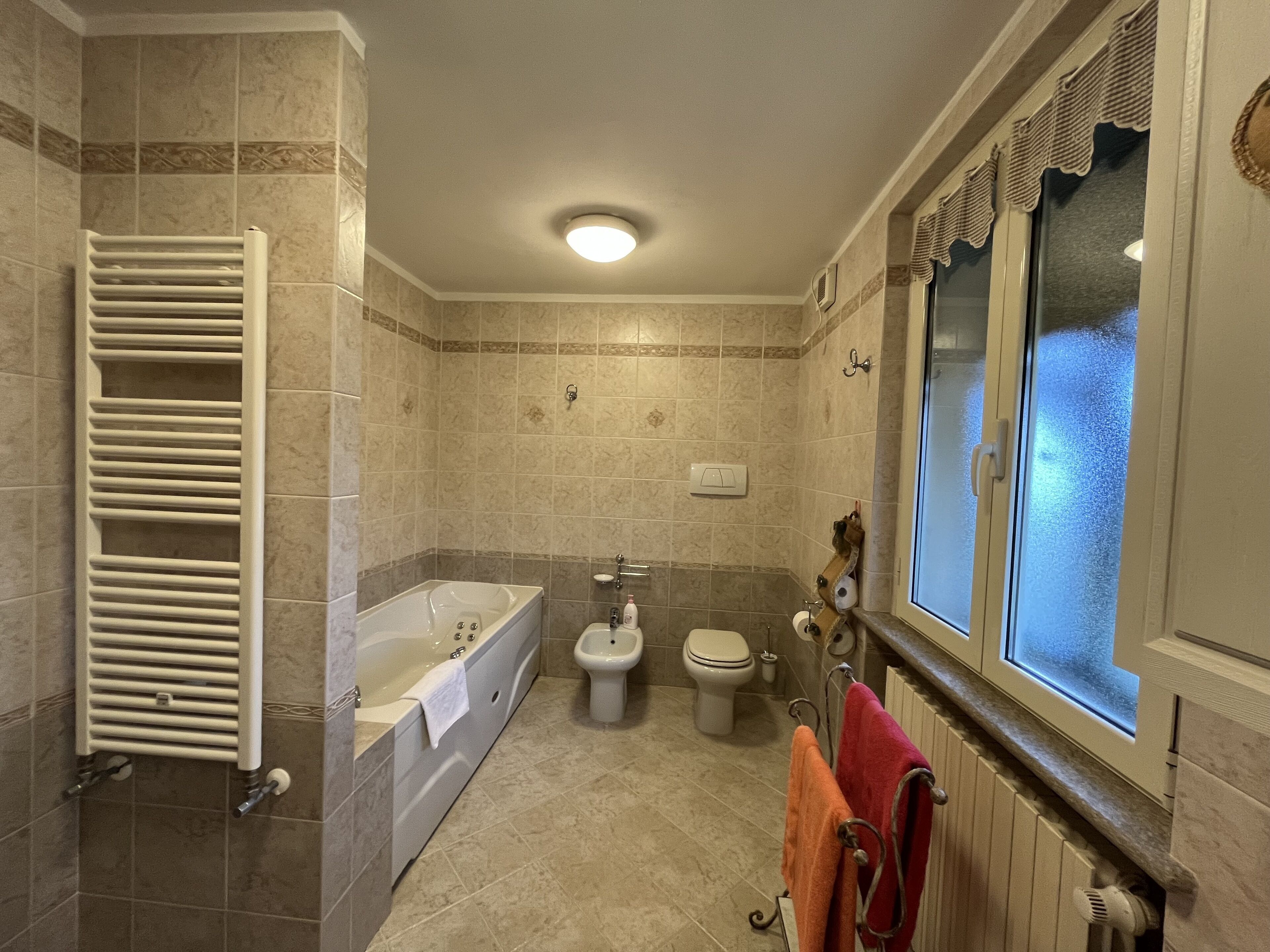 Et badeværelse med badekar, toilet, bidet og et vindue med udsigt.
