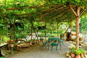 A covered outdoor seating area with a table and chairs, surrounded by potted plants and a wooden pergola. - Cascina Folletto (Pozzolo Formigaro)