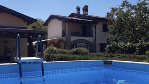 A swimming pool with steps leading into it, surrounded by a building with a tiled roof and a garden. - Cascina Folletto (Pozzolo Formigaro)