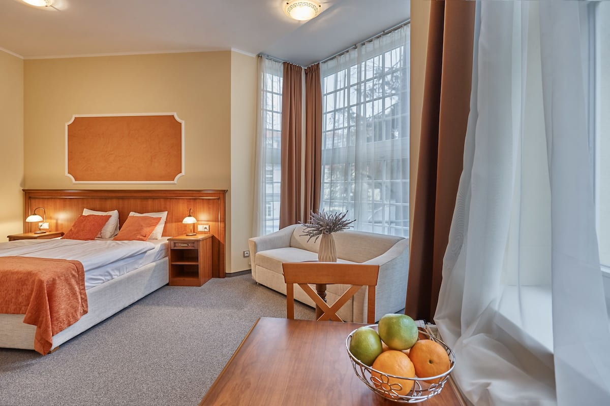 Quarto de hotel com cama, sofá, mesa de jantar com frutas e janela com cortinas.