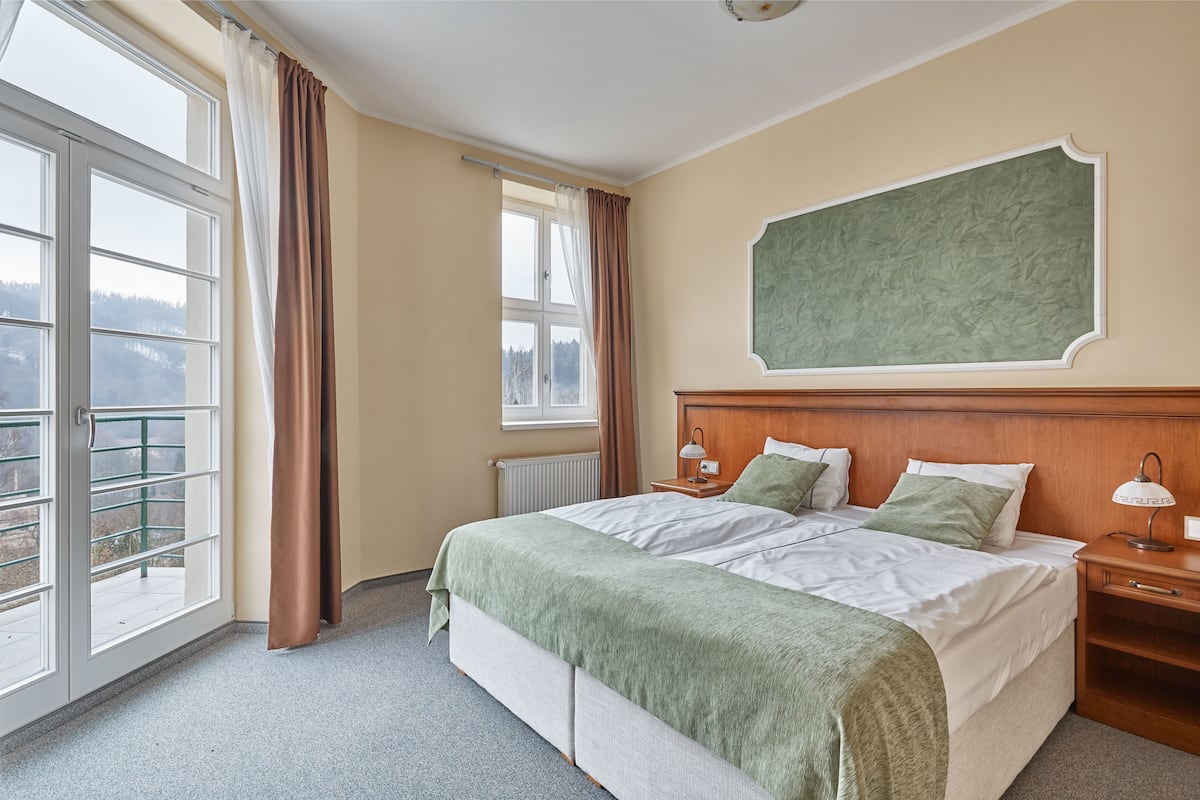 Quarto de hotel com uma cama grande, uma mesa de cabeceira, uma janela com cortinas e vista para o exterior.