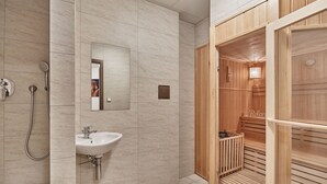 A modern bathroom with a sink, mirror, and wooden sauna. - Apart Hotel Akropolis (Karlovy Vary)