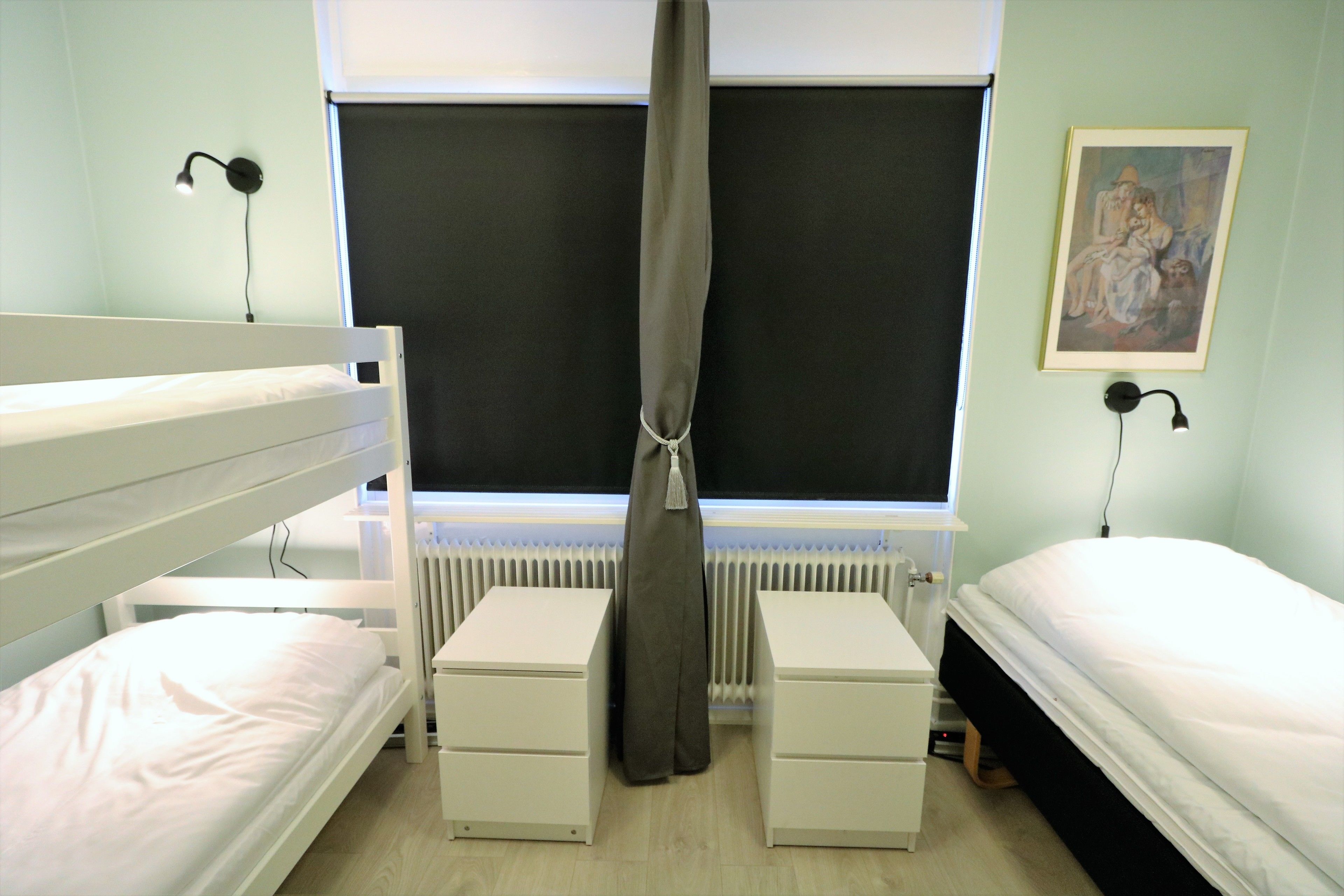 Un dormitorio con literas, un escritorio, una silla, un radiador y un cuadro en la pared.