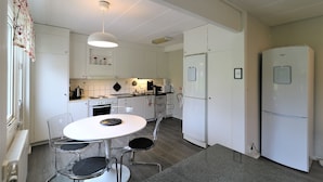 Una cocina compacta con armarios blancos, un refrigerador blanco, una mesa de comedor con sillas y una lámpara colgante.
