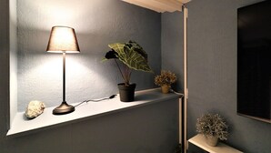 Una habitación con una estantería que sostiene una lámpara, una planta en maceta y un pequeño adorno.