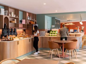 A modern kitchen with wooden cabinets, a coffee machine, and a counter with food items. - ibis budget Marne la Vallée Val d'Europe (Montevrain)