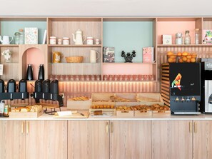 Mostrador de una panadería con diversos productos horneados, máquinas de café y una exhibición de naranjas.