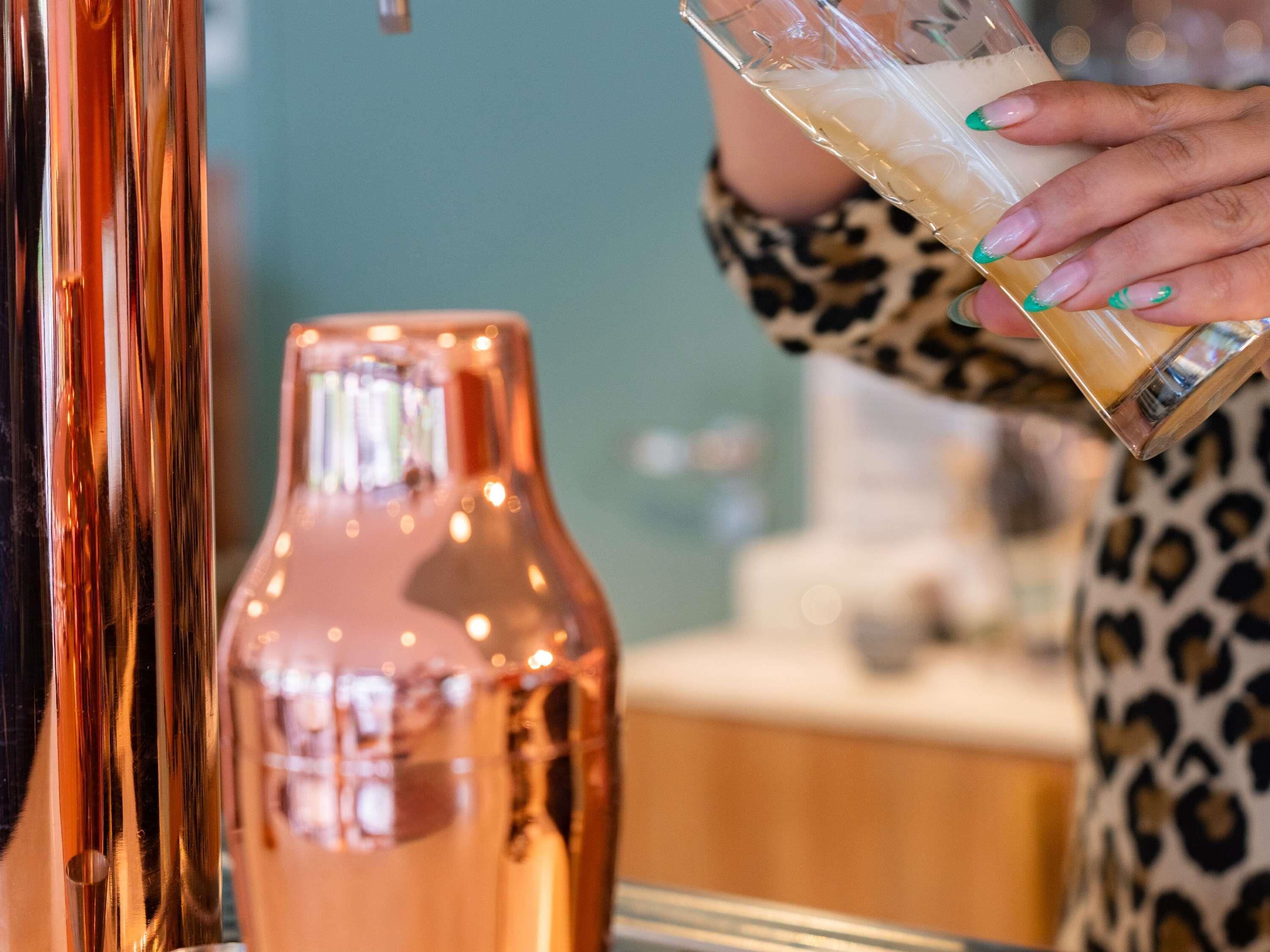 A person holding a glass with a beverage, a copper-colored bottle, and a leopard print garment.