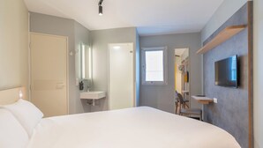 A bedroom with a bed, a bedside table, a TV mounted on the wall, a window, and a door. - ibis budget Marne la Vallée Val d'Europe (Montevrain)
