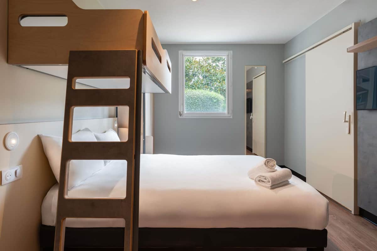 Habitación con literas, una mesita de noche, ventana con vista a follaje y un armario.