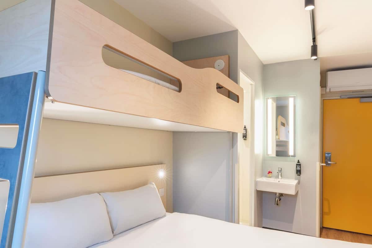 Habitación con literas, una mesita de noche, un espejo y un baño con lavamanos.