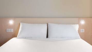 A neatly made bed with white linens, two wall-mounted light fixtures, and a wooden headboard.