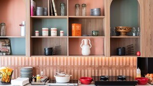 A kitchen with wooden cabinets, shelves with kitchenware, a stove, and various cooking utensils. - ibis budget Marne la Vallée Val d'Europe (Montevrain)