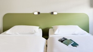 Habitación de hotel con dos camas individuales, ropa de cama blanca, cabecera verde y lámpara de pared.