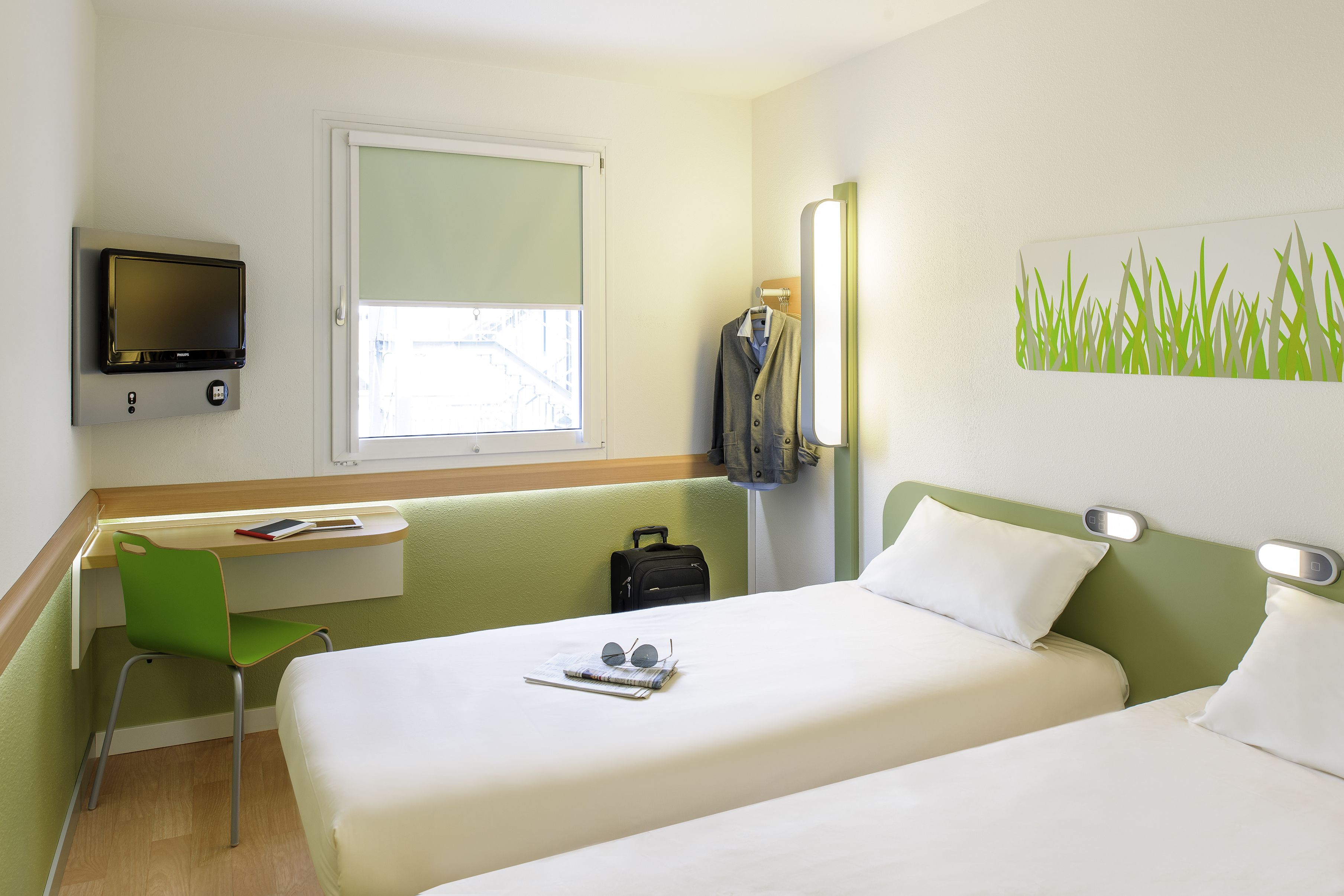 A hotel room with two beds, a desk with a chair, a television, and a window.