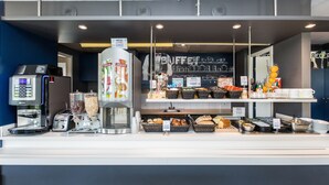 Mostrador de buffet con máquina de café, diferentes alimentos y cestas de pan.