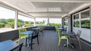 Un patio al aire libre con mesas y sillas, ventanas amplias y vistas del entorno.