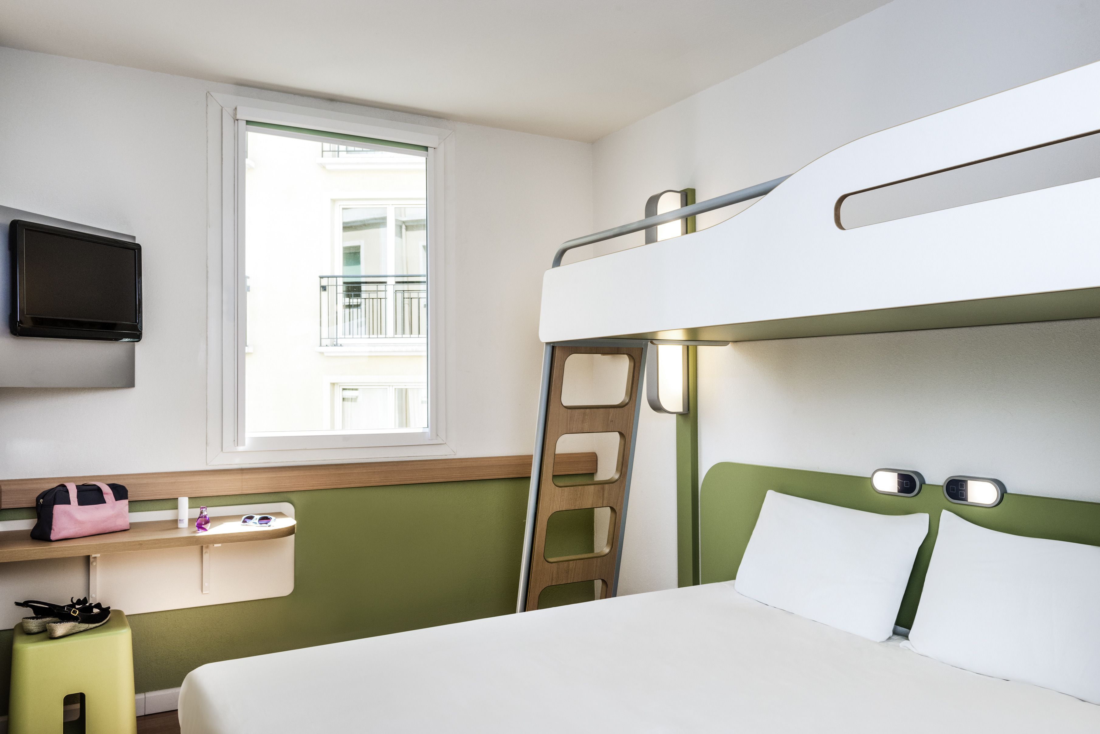 Habitación con literas, televisión, ventana, escalera y una mesita con una bolsa y zapatos.