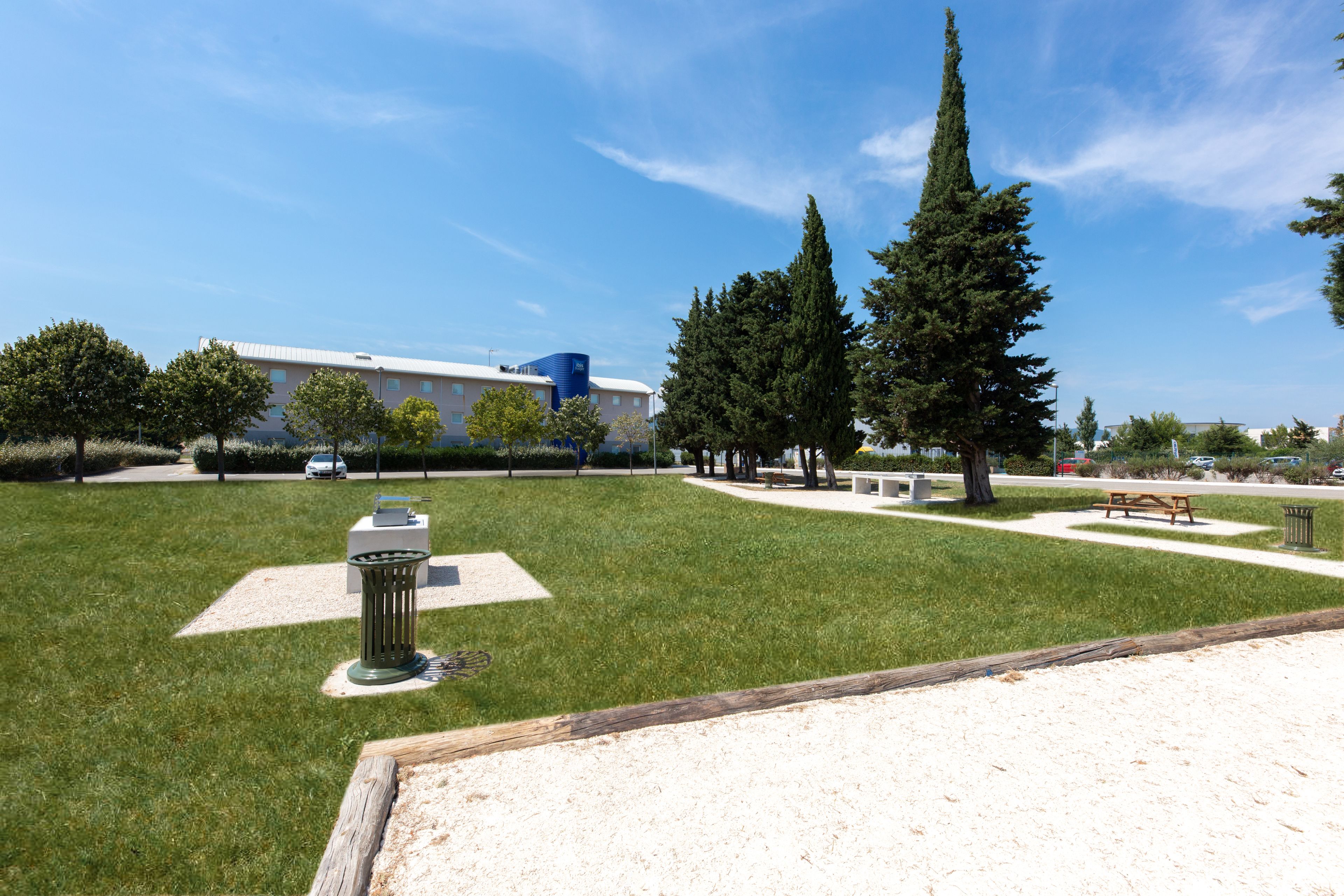 Un parque con césped, una mesa de picnic, bancos y un bote de basura.