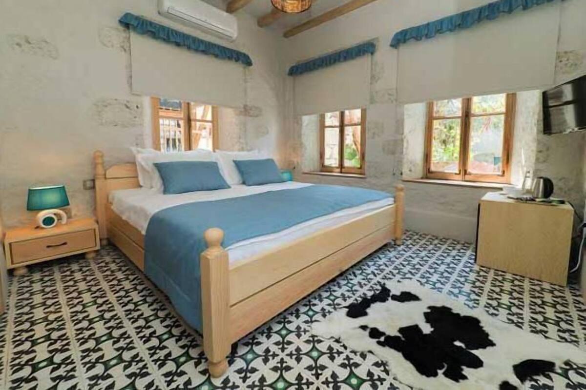 Un dormitorio con cama de madera, suelo estampado, alfombra de cuero de vaca y ventana con cortinas.