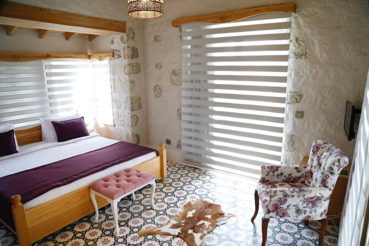 Un dormitorio con cama de madera, un banco, un sillón floral y suelo estampado.