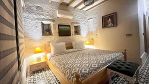 Een slaapkamer met een bed met een patroon, een nachtkastje met een lamp, een stoel en een wandplank met een schilderij.