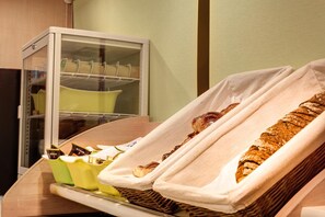 Una vitrina de panadería con pasteles y pan, un refrigerador y un estante con productos envasados.