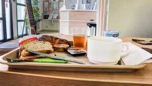 Una bandeja con un sándwich, una taza de té, un paquete de mantequilla y un pequeño recipiente de mermelada.