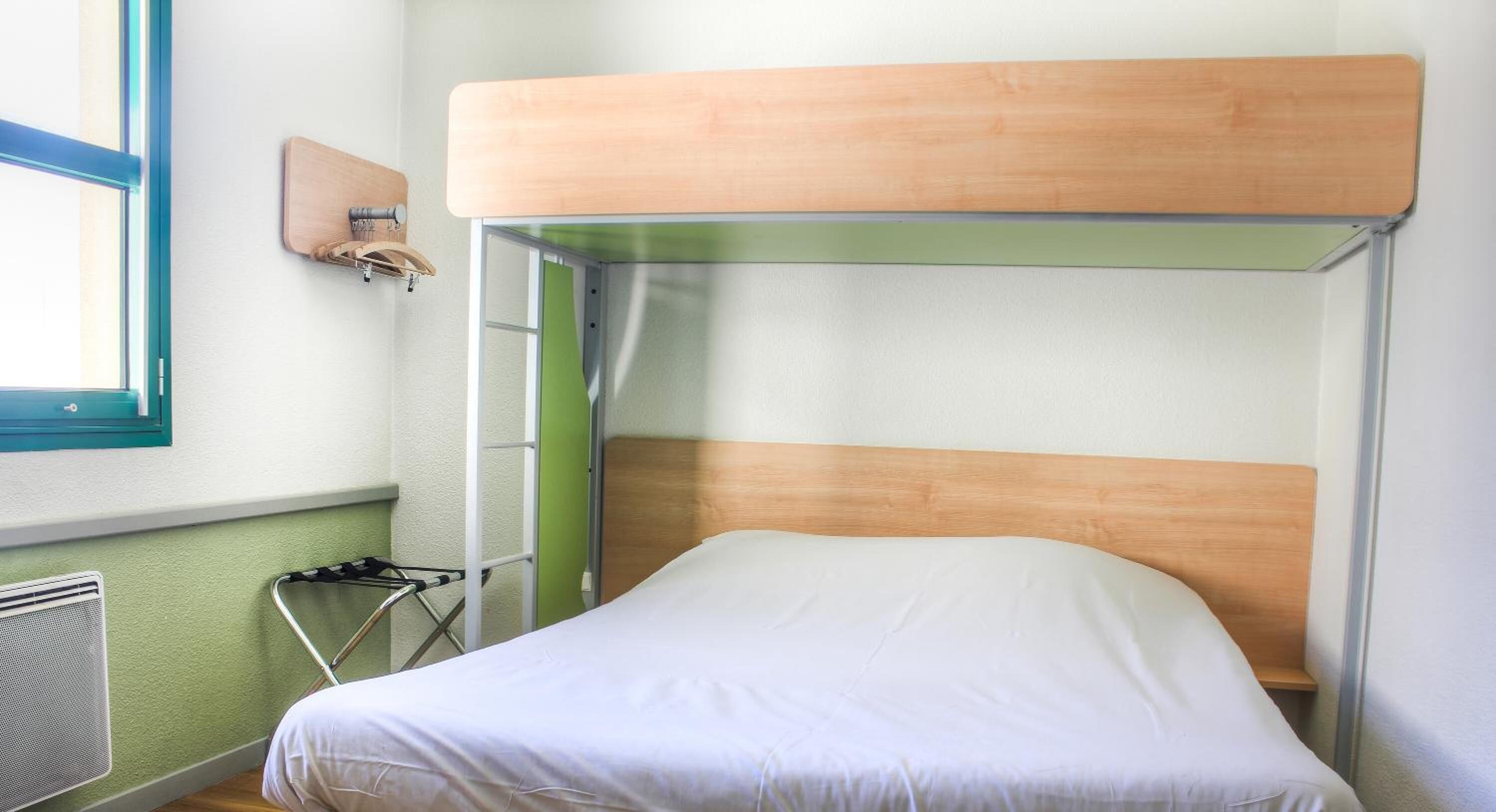 Una cama litera con cabecera de madera, escalera metálica y colchón blanco.