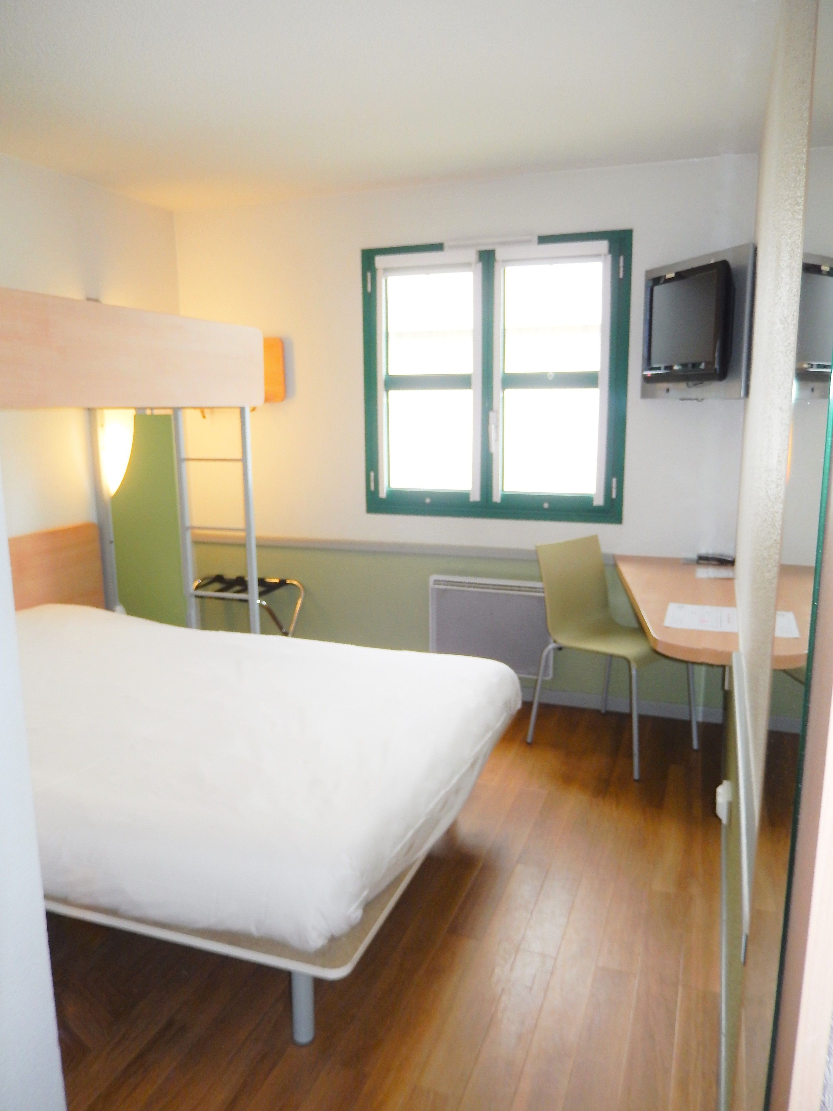 Une chambre avec un lit superposé, un bureau, une chaise, une télévision et une fenêtre.