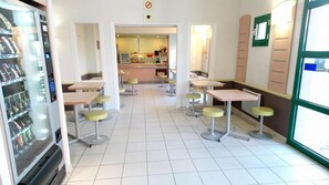 Una cafetería moderna y limpia con varias mesas y taburetes, una máquina expendedora y vistas a la calle.