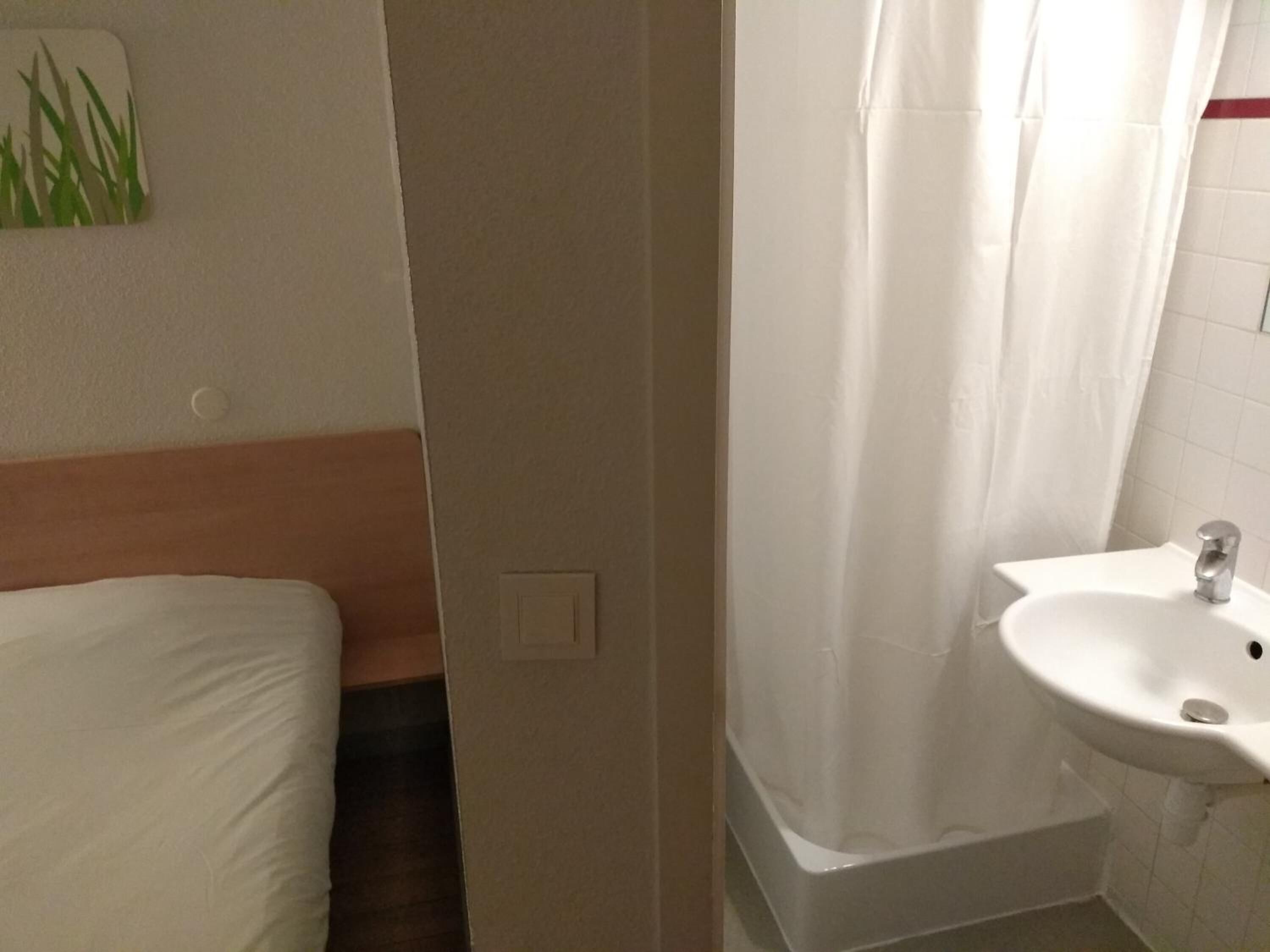 Ein Badezimmer mit Waschbecken, Duschvorhang und einem Bett mit weißer Bettwäsche.