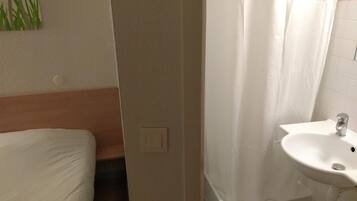 Ein Badezimmer mit Waschbecken, Duschvorhang und einem Bett mit weißer Bettwäsche.